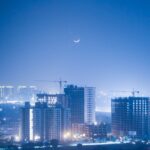 Illuminated cityscape of Greater Noida at night with a crescent moon enhancing the urban skyline.